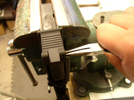 Holding the detent in like so will allow the other hand to use the pivot pin to push the detent fully into the hole, allowing the pin to move left into its loops, also retaining the detent underneath.