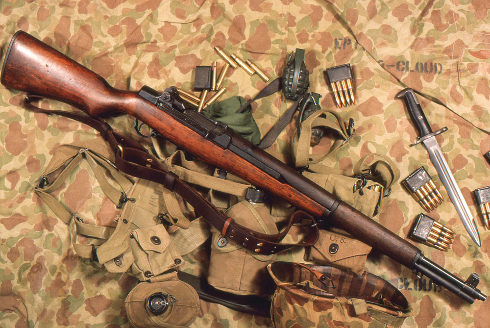 ??) The author’s 1943 M1, about 1986, by which time the barrel had been replaced, displayed and photographed here with vintage ammo and U.S.M.C. militaria, on a World War II vintage camouflaged shelter half.